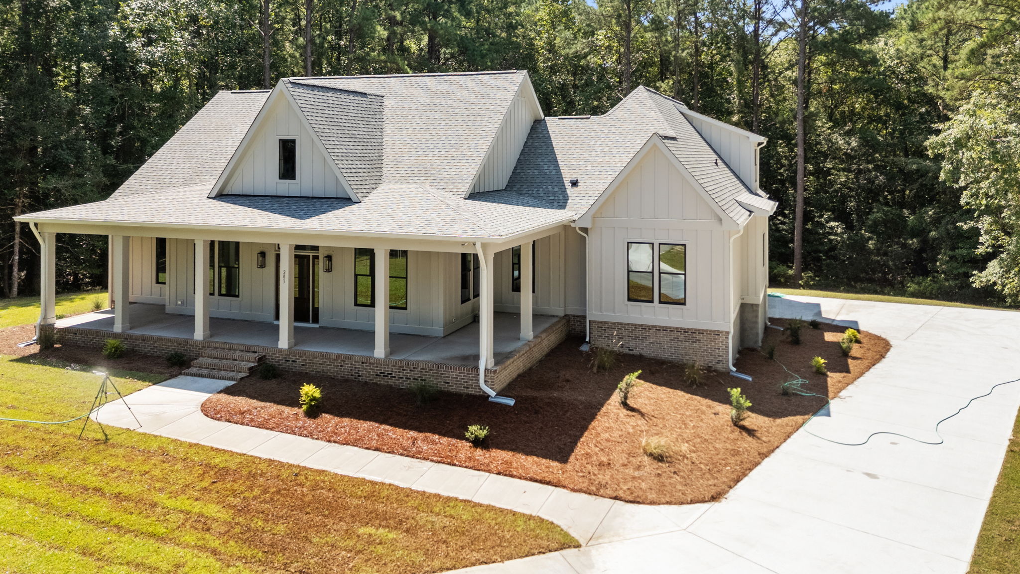aerial view of front exterior house with cream hardiboard siding, side-load garage, black windows, and wraparound front porch