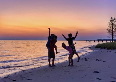 People jump with joy on the beach as the sun sets behind them.